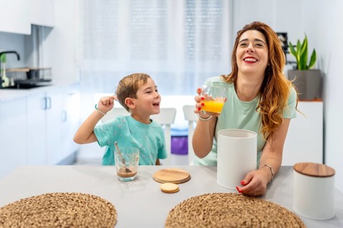 Mother and boy laughing while eating breakfast before going to school at home