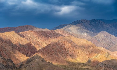 Red and orange mountains in atmospheric light, dramatic cloudy sky, mountain landscape near