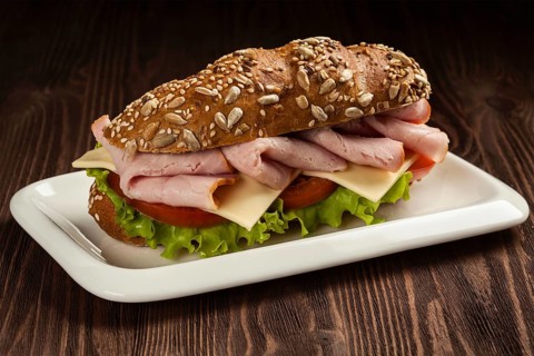 Ham sandwich with lettuce, cheese, tomato on plate on wooden table
