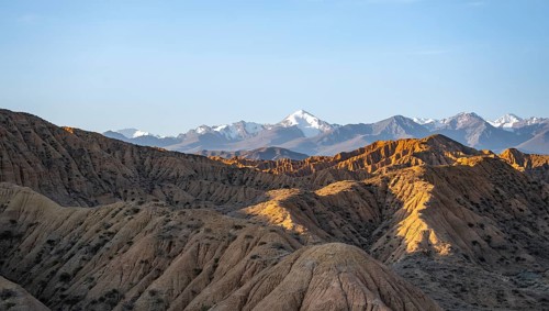 Landscape of eroded hills at sunrise, badlands, white mountain peaks of the Tian Shan Mountains in