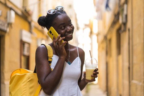 Young african woman talking with the mobile and drinking milkshake stranding on the street