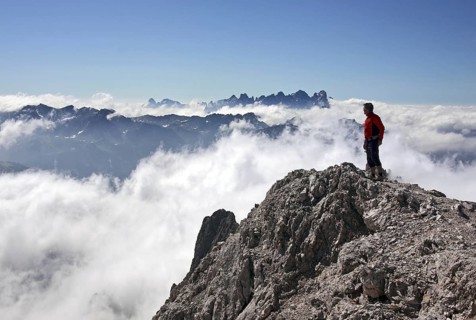 Mountaineer looking from the Cima Scalieret over blanket of clouds and mountain peaks of the