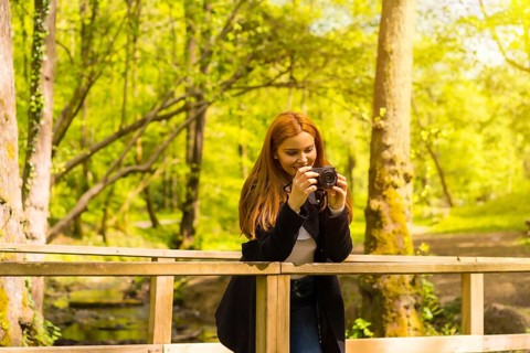 Woman photographer with a black jacket enjoying in an autumn park, taking pictures on a wooden