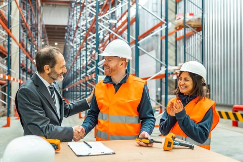 Manager shaking hands with a warehouse worker after closing a deal, his colleagues clapping hands,