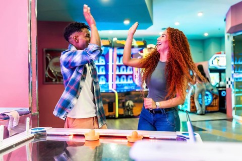 Two friends giving high five while enjoying a game of air hockey in a vibrant entertainment center,