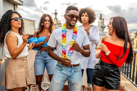 Happy latin man with Hawaiian necklace dancing with friends in outdoor rooftop party