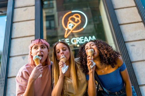 Low angle view photo of three diverse female friends enjoying eating a delicious ice cream outside