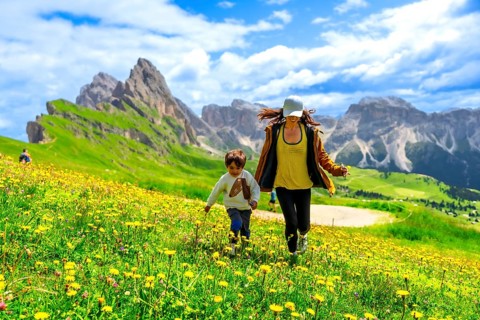 Mother and son running through a field of wildflowers in the italian dolomites mountains, enjoying