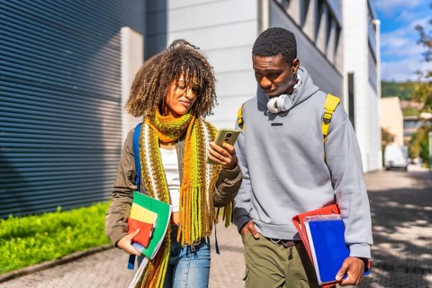 Multi-ethnic students checking information with the mobile phone walking along the university