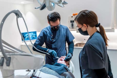 Dentist wearing magnifying glasses and face mask performing a dental procedure on a senior female