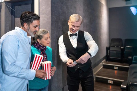 Couple entering a movie theater, holding popcorn buckets while the usher checks their tickets,