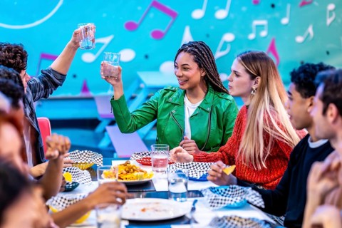 Multiethnic friends enjoying a meal and drinks at a bowling alley restaurant, celebrating their