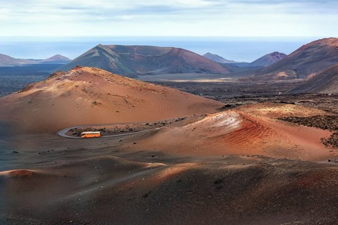 Orange-coloured coach with tourists drives through the fire mountains of Timanfaya National Park,