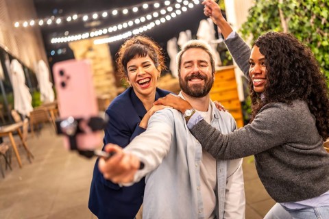 Happy hipster man recording online video blog with two female diverse friends at night party