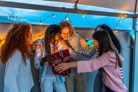 Happy millennial multi-ethnic friends celebrating birthday party in an urban rooftop at dusk