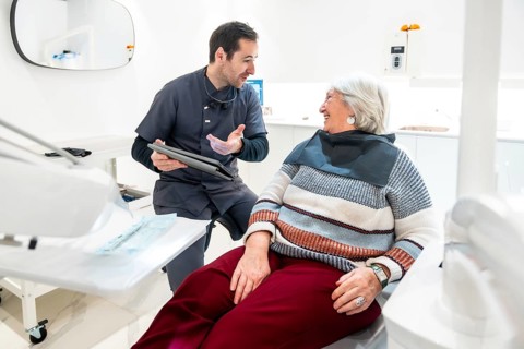 Dentist is explaining something on a tablet to a senior female patient during a consultation in a