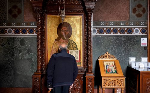 Elderly man praying in front of an image of a saint, from behind, interior view of Hagia Sofia