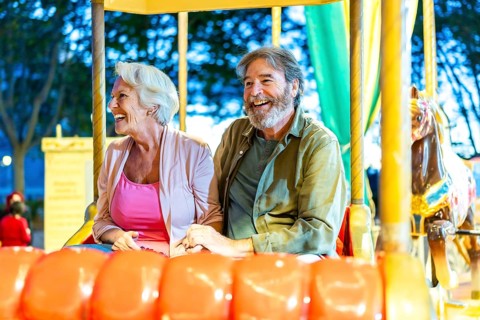 Happy caucasian senior couple enjoying a ride with carousel at night in the city