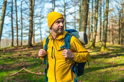 Male hiker in a bright yellow jacket and blue backpack walking through a lush forest, soaking up