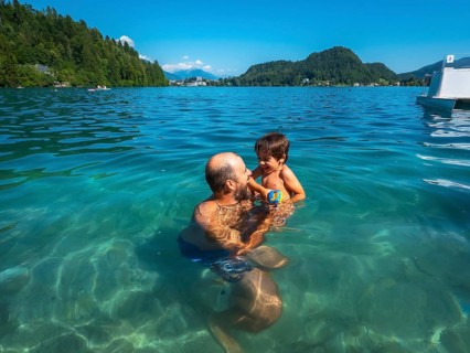 Father and son having fun swimming in the clear waters of lake bled, surrounded by the beauty of