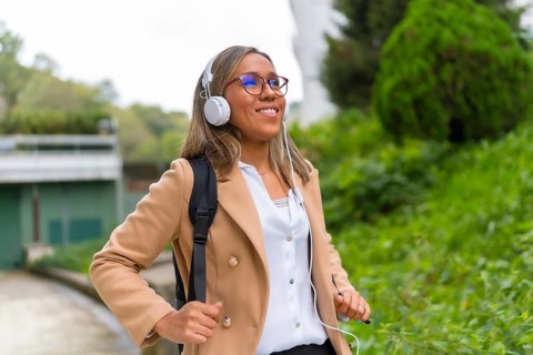 Portrait of a happy latin businesswoman listening to music commuting in the city walking down a