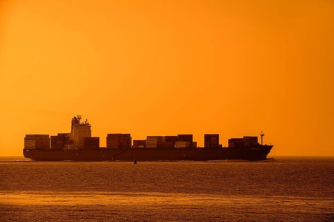 Container ship, containership Amalthea, loaded with containers silhouetted against orange sunset