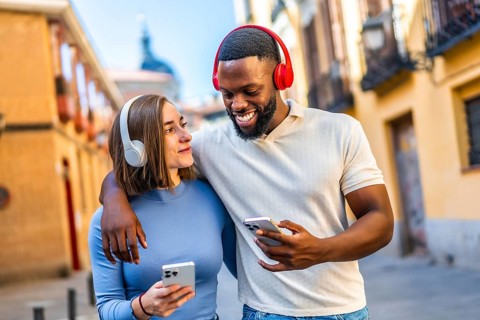 Happy young multi-ethnic couple using mobile and listening to music walking together in the city