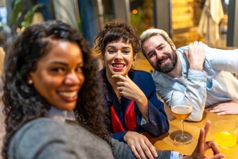 Latin woman and friends taking selfie while sitting on bar enjoying beer together