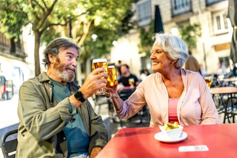 Happy relaxed senior couple toasting with beer in sidewalk cafeteria at night