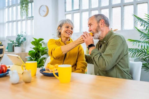 Senior woman feeding her husband in a romantic gesture in the morning sharing breakfast at home