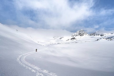 Ski tourers ascending through a picturesque snow-covered mountain landscape with peaks, ascent to
