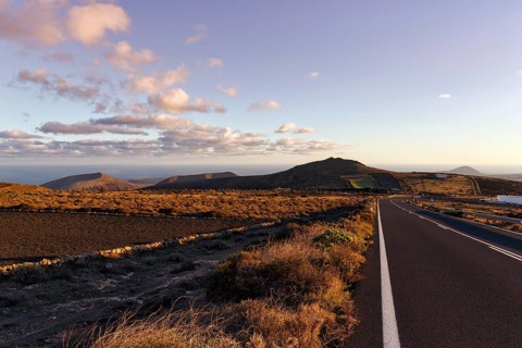 Road leads through hilly volcanic landscape, Famara Mountains, evening sky, Cumulus, Los Valles,