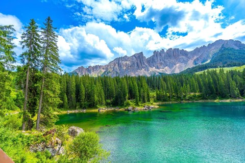 Emerald waters of lake carezza reflecting latemar mountain range, surrounded by lush pine forest