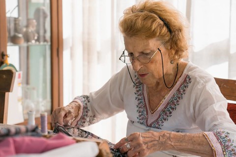 Senior seamstress stitching fabric with concentration in her home workshop, surrounded by colorful