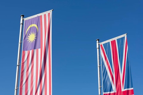 Malaysia and British flags fly against a clear blue sky