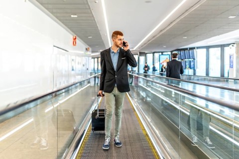 Businessman pulling suitcase and talking on smartphone while using airport moving walkway