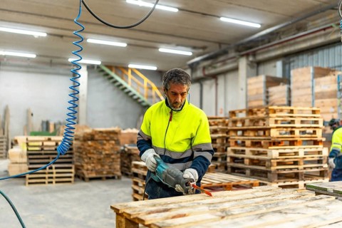 Adult caucasian man worker repairing broken pallets in a recycling plant workshop using compressed