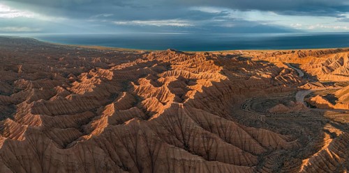 Riverbed runs through a landscape of eroded hills, badlands at sunset, Issyk Kul Lake in the