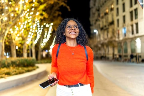 Young woman enjoying an evening stroll through a vibrant, illuminated city, engaging with her