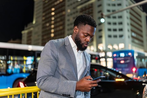 Young businessman using smartphone on a city street at night, with blurred traffic and buildings in