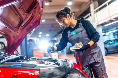 Young female mechanic wearing overalls and protective glasses is checking the oil level of a car