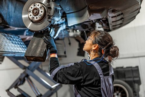 Skilled female mechanic working under a lifted car, inspecting and repairing the brake system in a