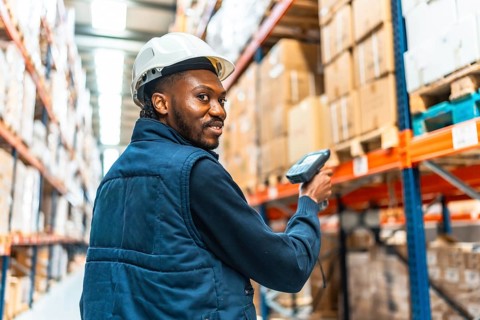 Happy african worker turning to smile while scanning packages in a large warehouse