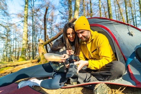 Couple of hikers reviewing photos on their camera while having a meal in front of their tent during