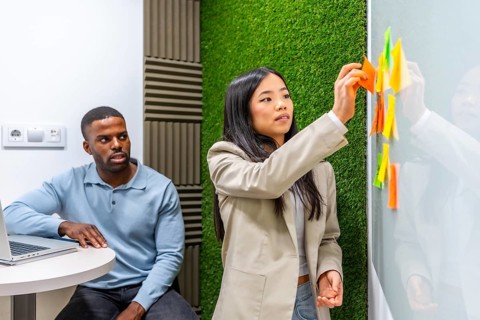 Businesswoman sticking notes on whiteboard during a brainstorming session with her colleague in a