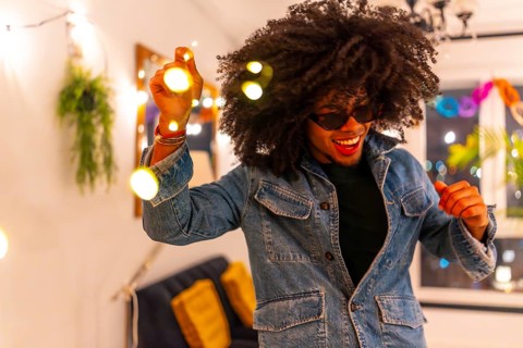 Excited latin young man with curly hair dancing playing with decoration lights at home party