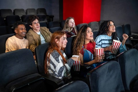 Group of excited friends enjoying a movie and eating popcorn in a cinema, sharing a fun and