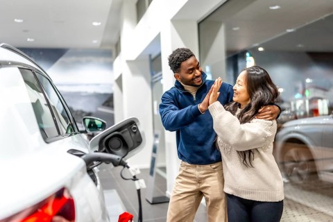 Happy multiethnic couple celebrating their new electric car purchase with a high five at the