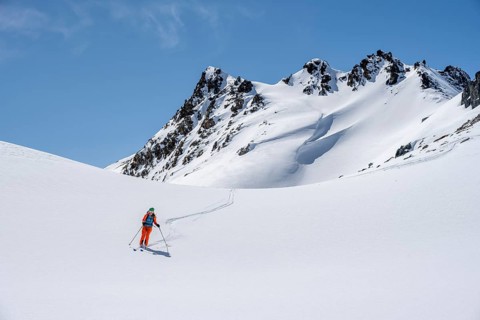 Ski tourer on the descent, minimalist winter landscape, white snow and dark mountains on the
