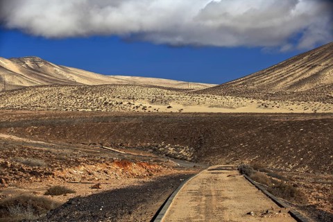 Lonely road in front of a dune landscape under a cloudy sky, Pajara, Fuerteventura, Canary Islands,